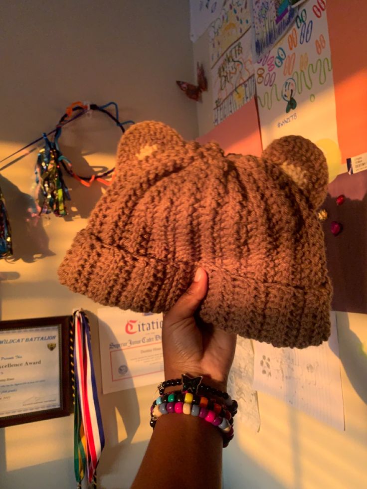 a person holding up a brown teddy bear hat