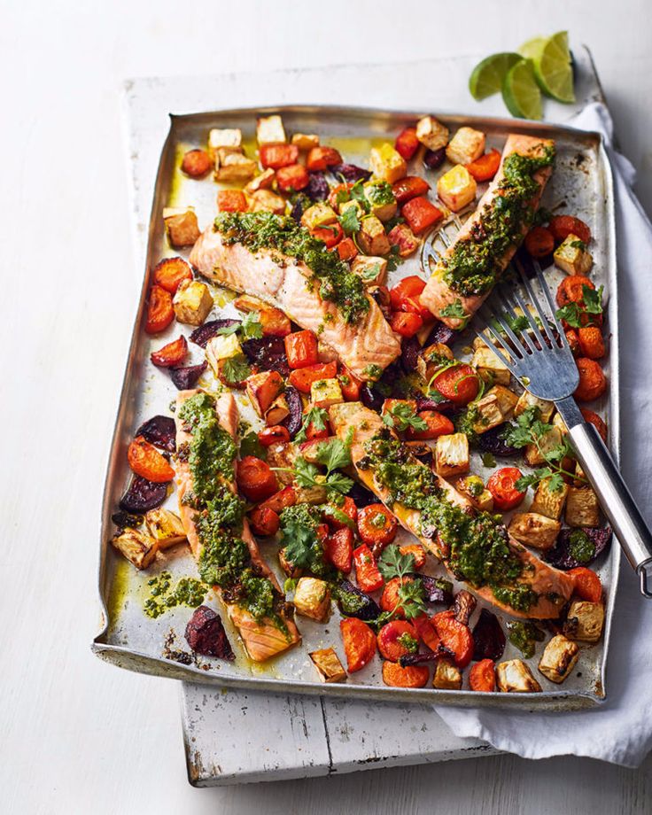 a pan filled with salmon and vegetables on top of a white table next to a fork