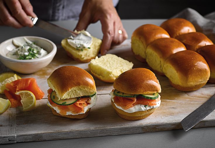 several sandwiches are on a cutting board with dips and lemon wedges next to them