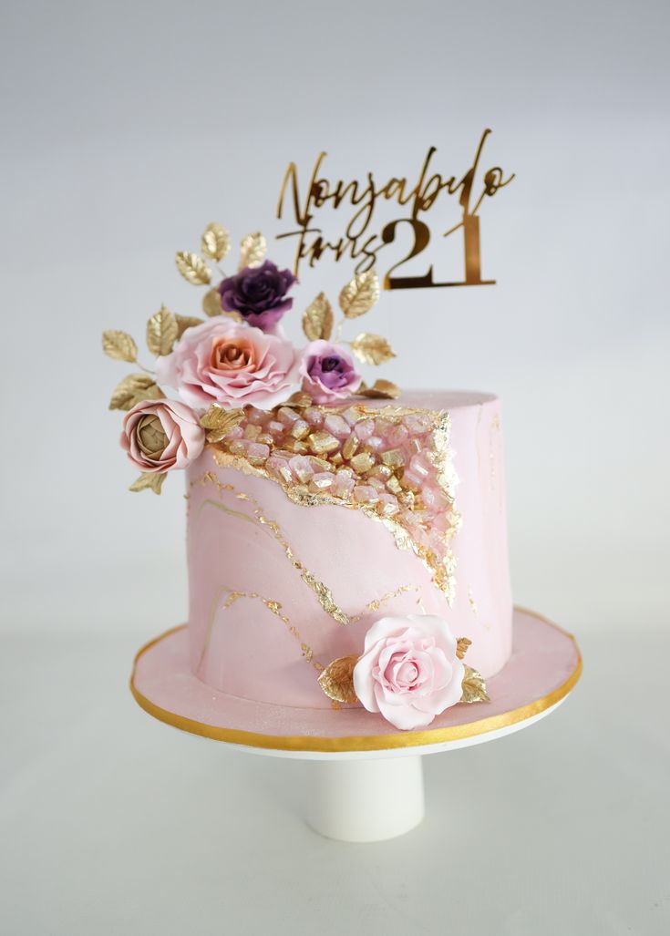 a pink and gold cake with flowers on the top is decorated with a number one