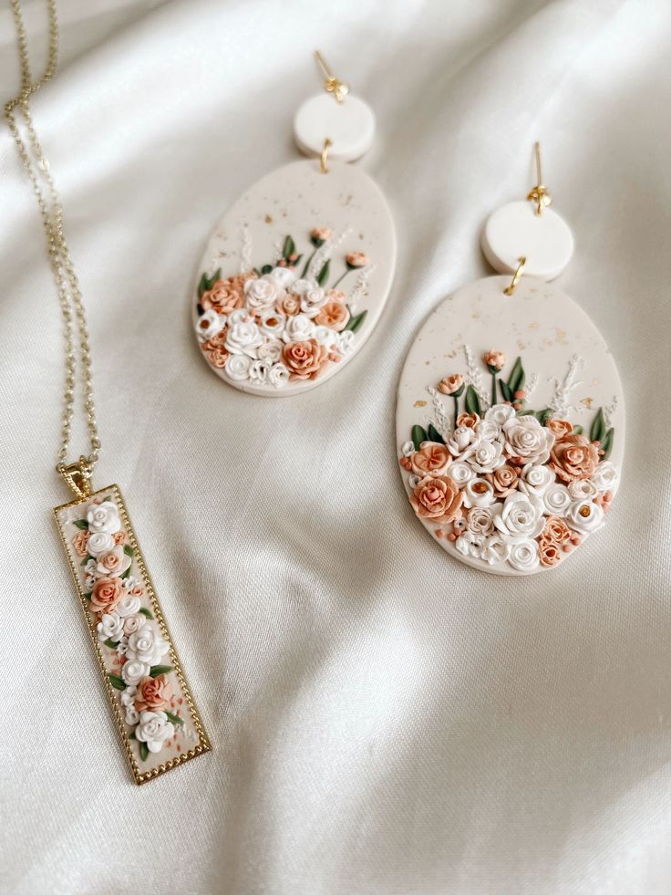 three necklaces with flowers on them sitting on a white cloth covered bed sheet,