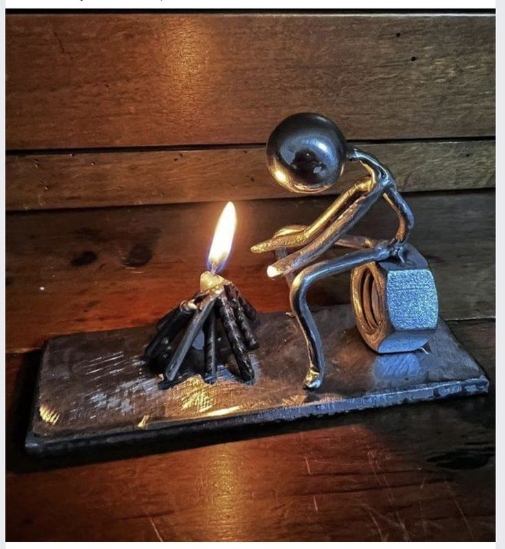 a small metal figurine sitting on top of a table next to a lit candle