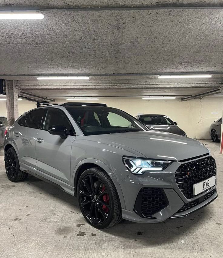 a grey audi suv parked in a parking garage next to other cars on the street