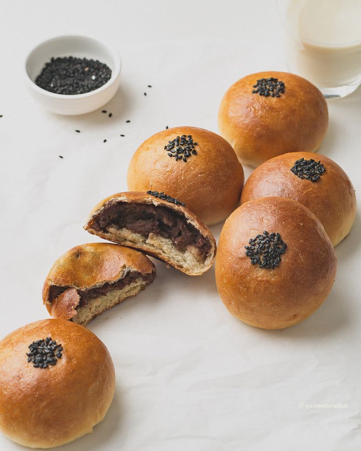 several rolls with black sesame seeds cut in half on a white surface next to a glass of milk