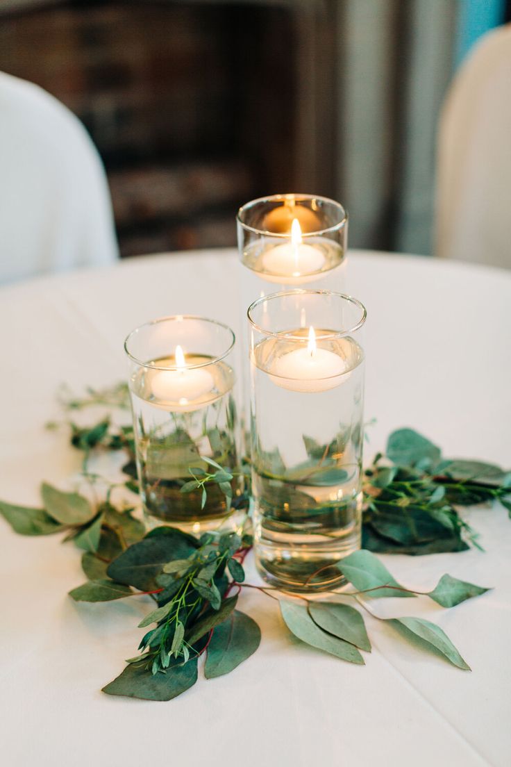 candles are placed in glass vases with greenery