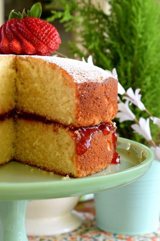 two slices of jam filled vanilla layer cake on a green plate with flowers in the background