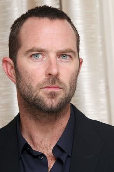 a close up of a person wearing a suit and tie with blue eyes looking at the camera