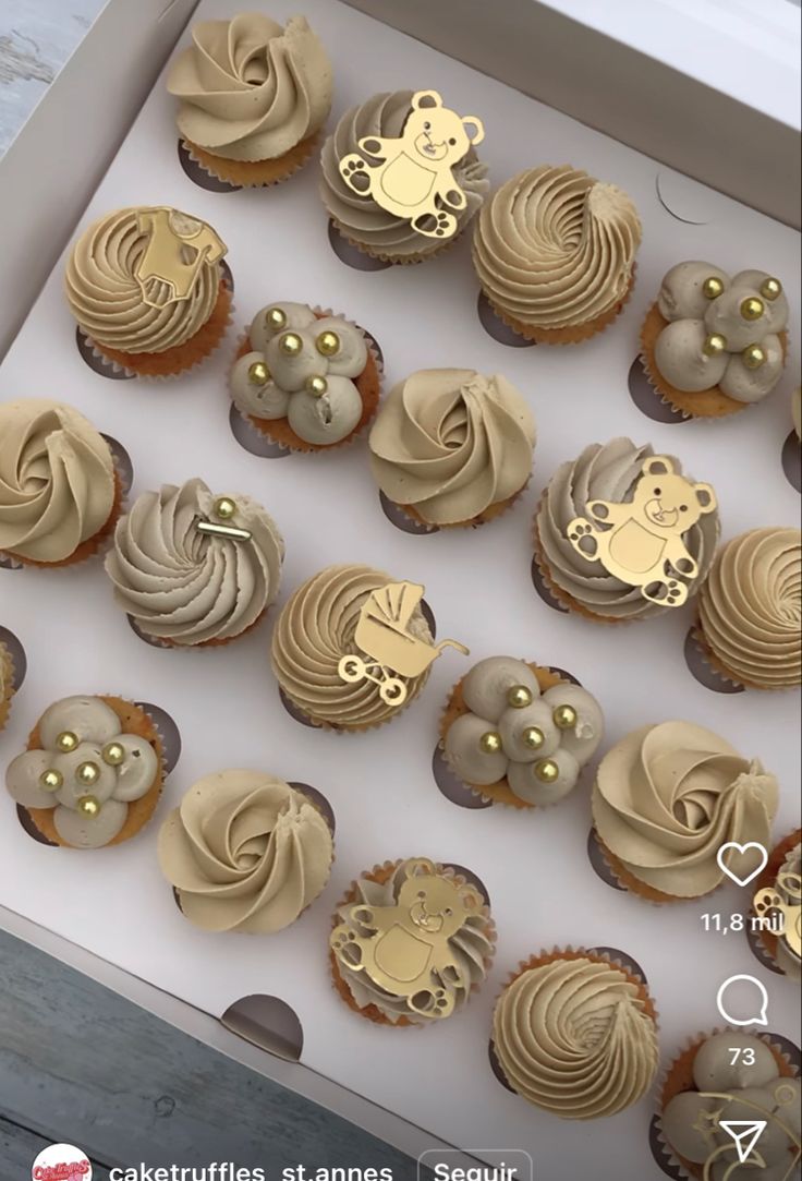 there are many cupcakes in the box with gold decorations on them that look like animals