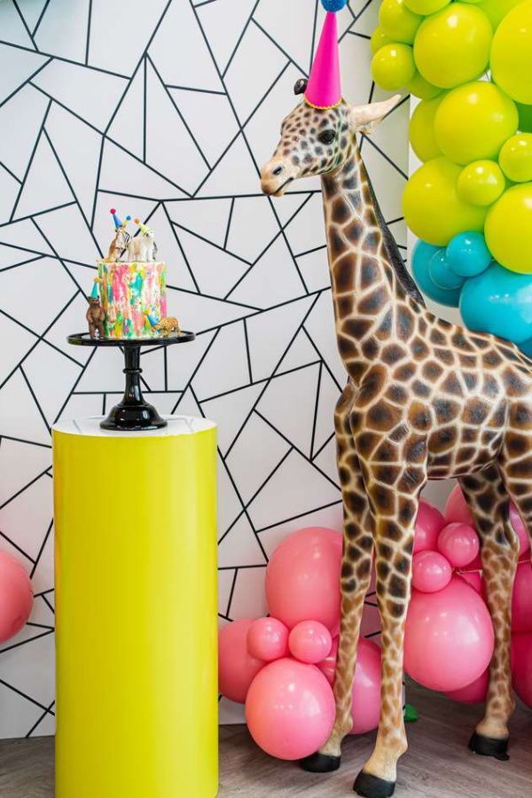 a giraffe standing next to a birthday cake and balloons