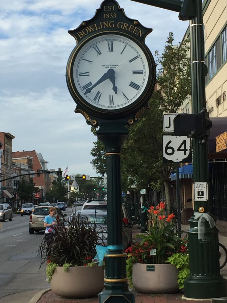 a clock on a pole in the middle of a street with potted plants next to it