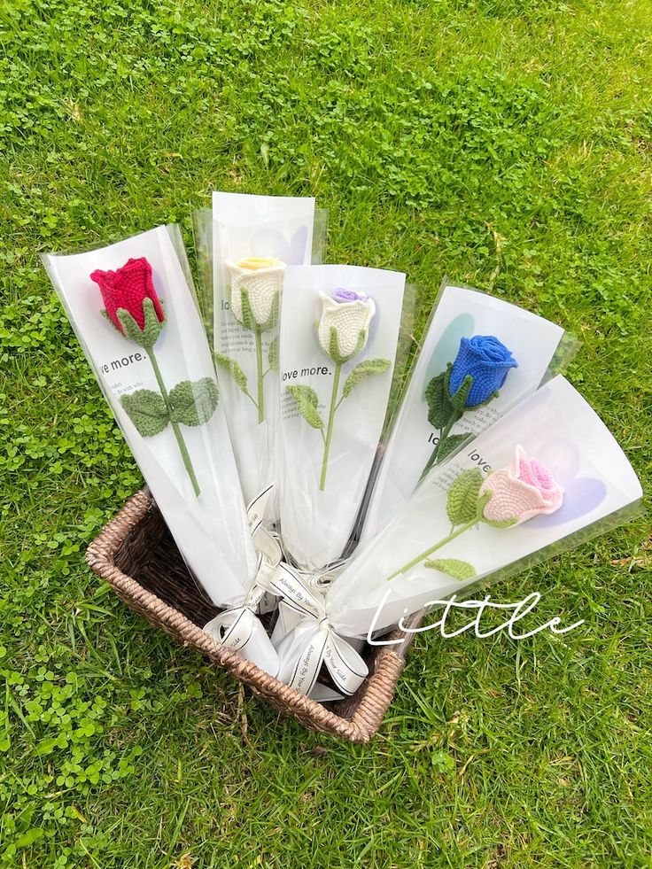 five different colored flowers are placed in a basket on the grass, and one is wrapped in cellophane