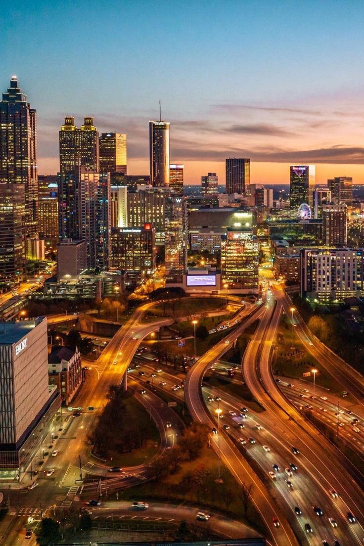 an aerial view of a city at night with cars driving on the road and buildings in the background