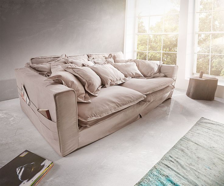 a couch sitting in front of a window next to a rug and book on the floor