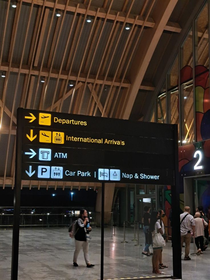 people are standing in front of an airport sign with directions to the destinations on it