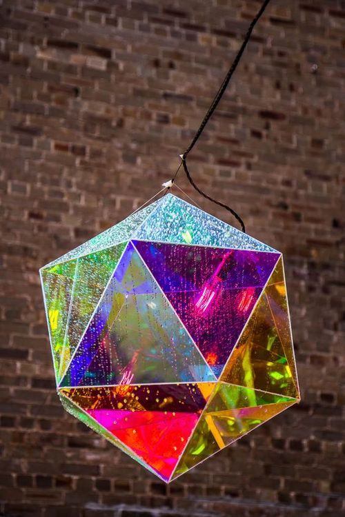 a multicolored diamond hanging from a string in front of a brick wall