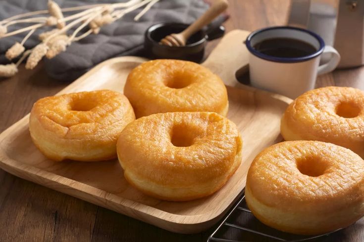 four doughnuts on a wooden tray next to a cup of coffee