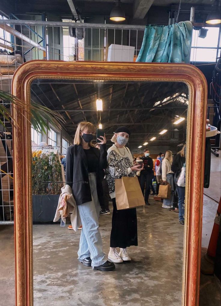 two people standing in front of a mirror with a face mask on and shopping bags