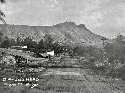 an old black and white photo of a dirt road with mountains in the back ground