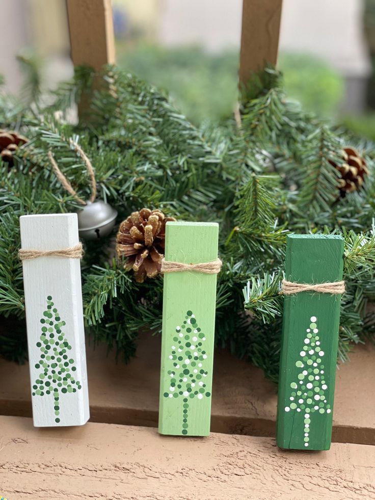 three wooden christmas trees are tied with twine and placed in front of pine cones