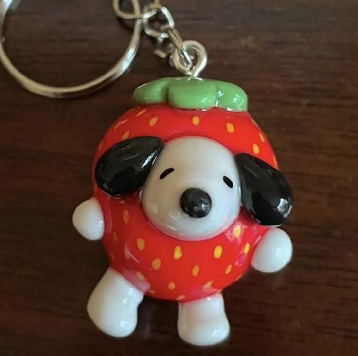 a keychain with a dog wearing a strawberry on it's head, sitting on a table