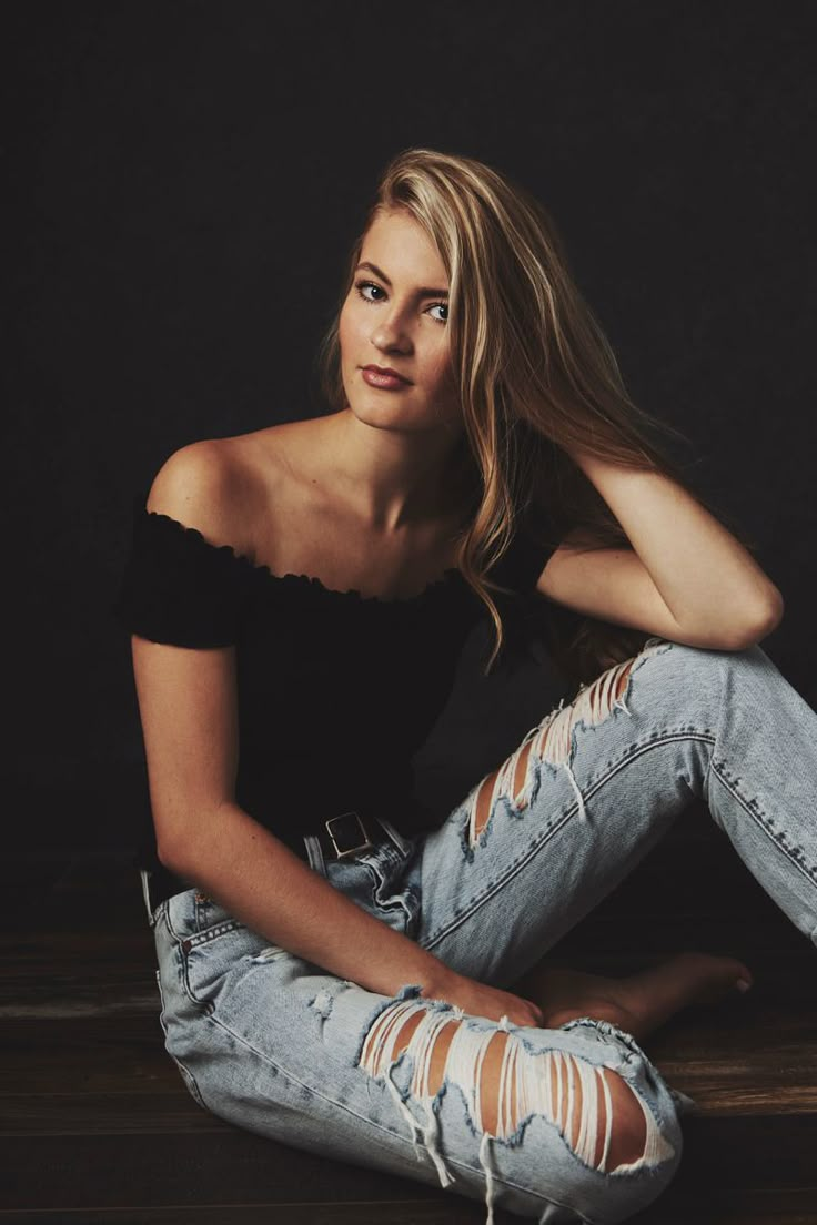 a woman sitting on the floor in ripped jeans and black top with her hair blowing back