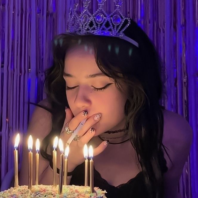 a woman blowing out candles on a cake with her hand in her mouth while wearing a tiara