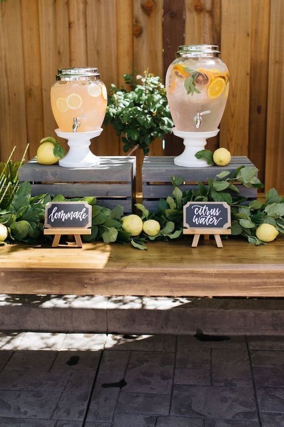 two vases sitting on top of a wooden table with lemons and greenery