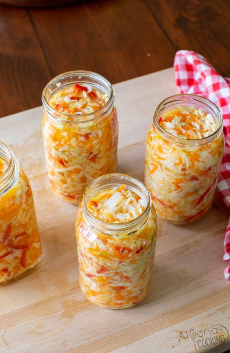 four jars filled with food sitting on top of a wooden cutting board next to a red and white checkered napkin