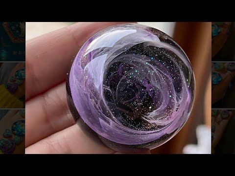 a hand holding a purple glass ball with stars on it