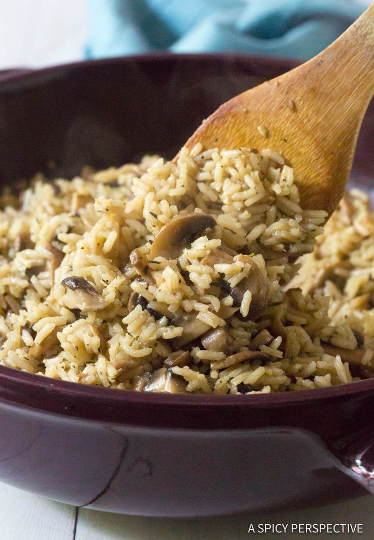 a bowl filled with rice and mushrooms next to a wooden spoon on top of a table