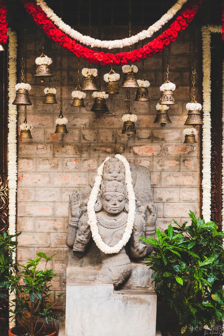 a statue in front of a brick wall with bells hanging from it's sides