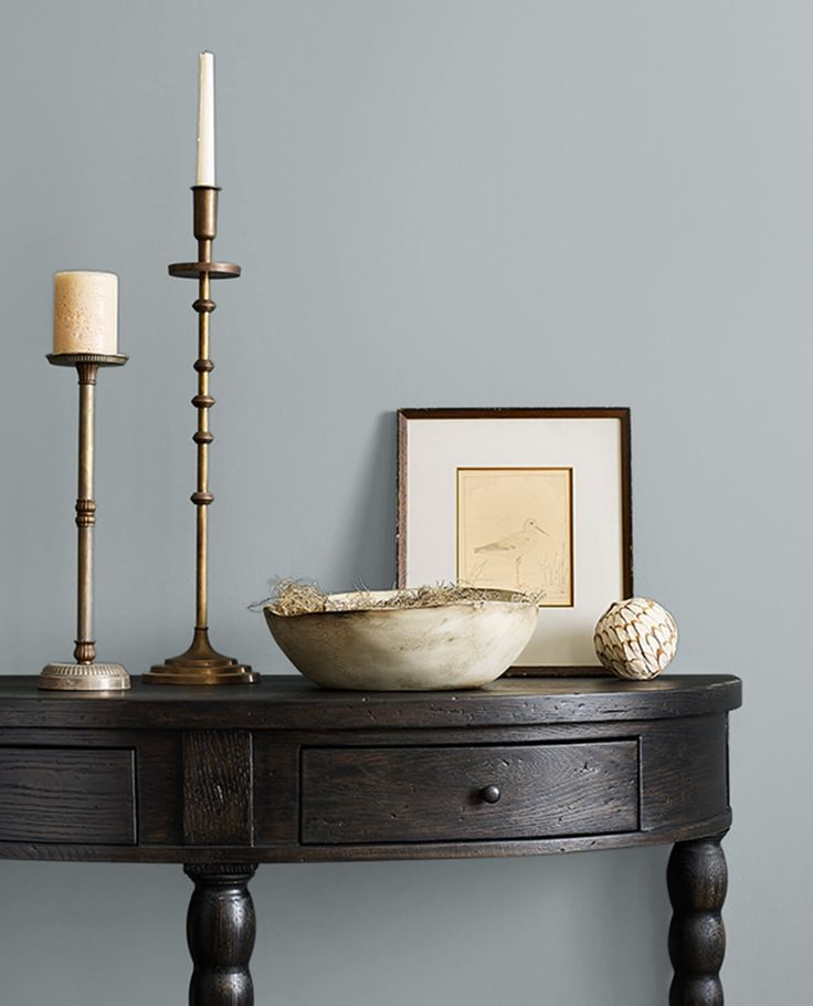 a wooden table topped with a bowl and two candles next to a framed picture on the wall