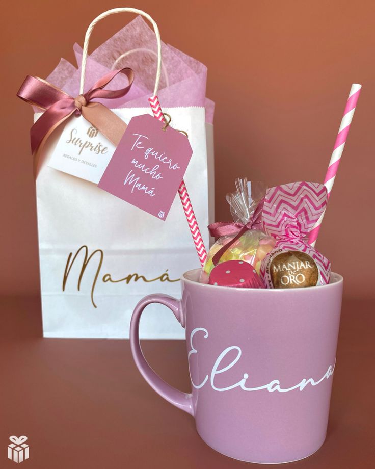 a pink coffee mug filled with candy and candies next to a white shopping bag