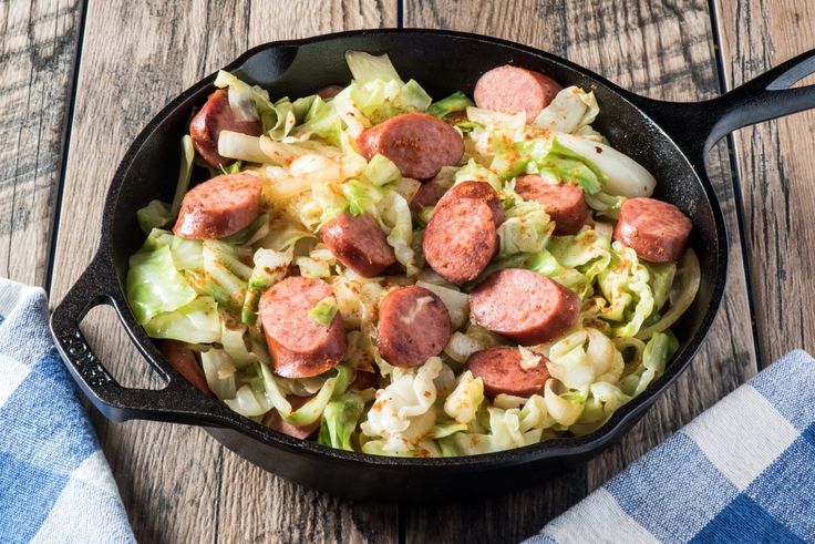 sausage and cabbage in a skillet on a wooden table