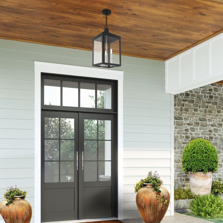 two large vases with plants are on the front porch next to an entry door