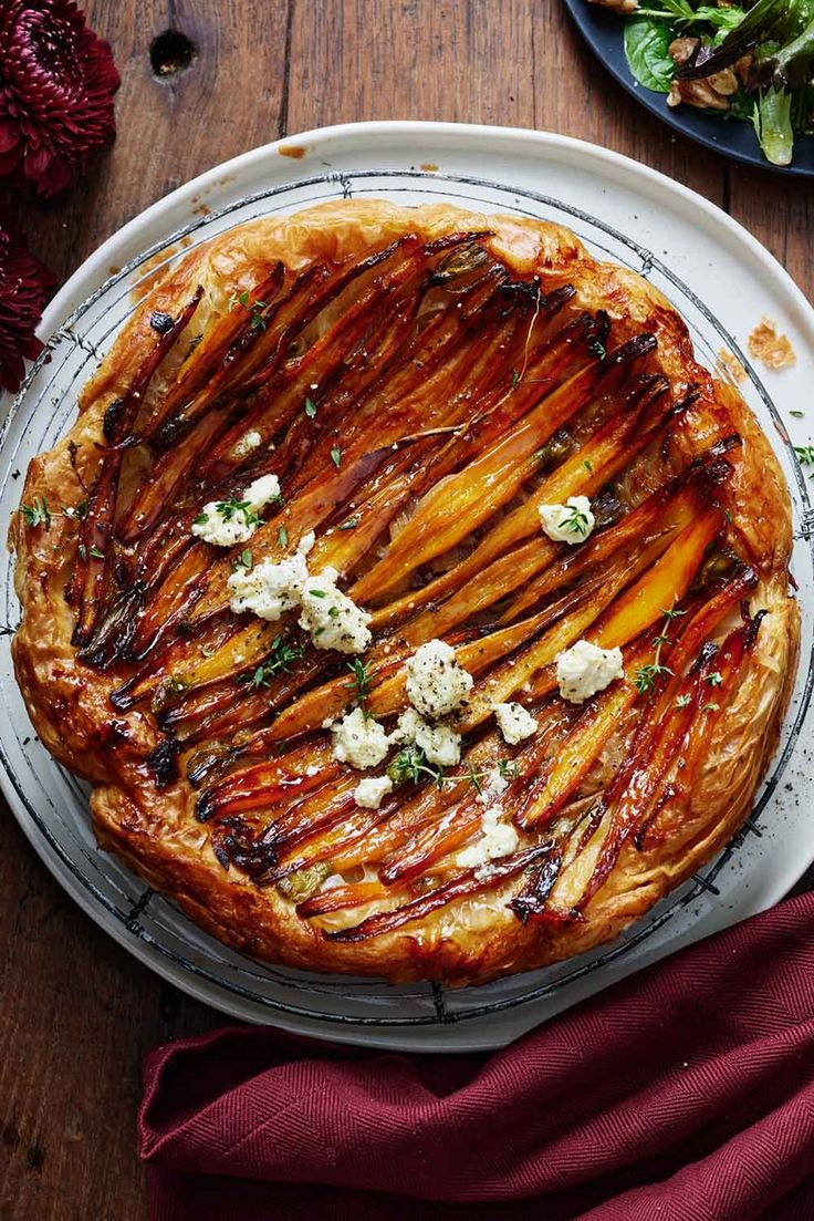 a pie on a plate topped with cheese and other toppings next to a bowl of salad