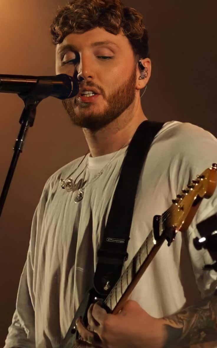 a man that is standing up with a guitar in front of him and singing into a microphone