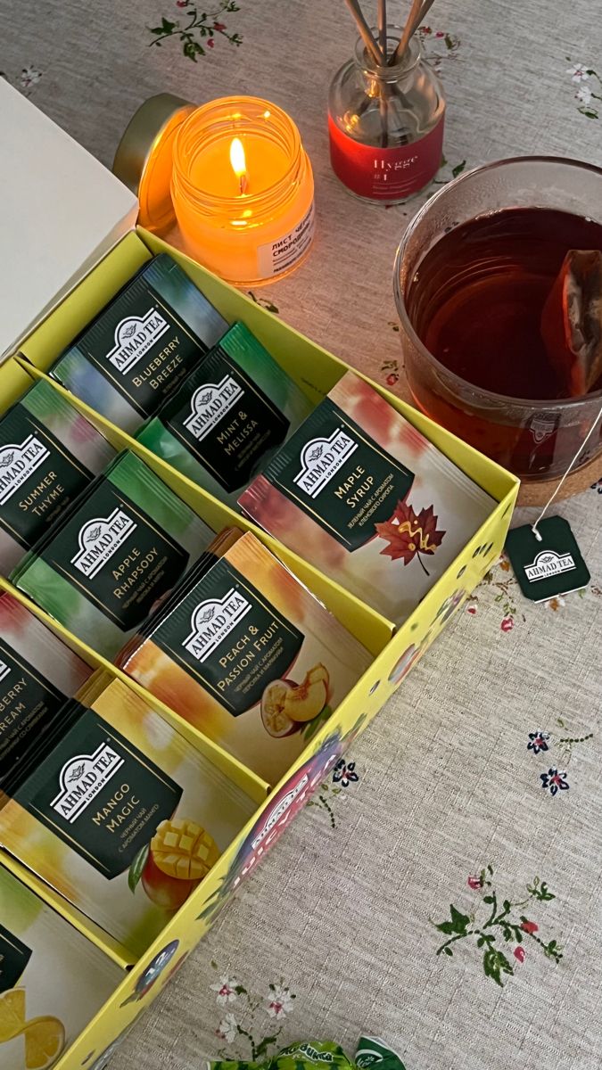 candles and teas sit on a table next to an open box with several different types of tea in it