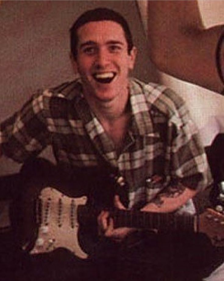 a man sitting on top of a bed holding an electric guitar in his right hand