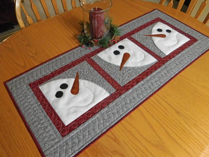 a quilted table runner with two snowmen on it and a candle in the center