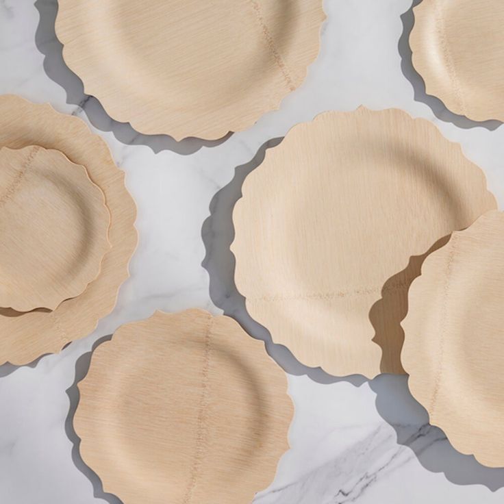 four wooden plates with scalloped edges on a white marble countertop, one is empty