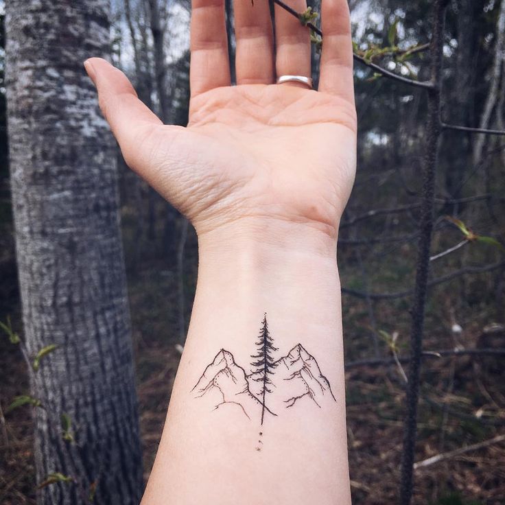 a person's hand with a small tattoo on the wrist and mountains in the background