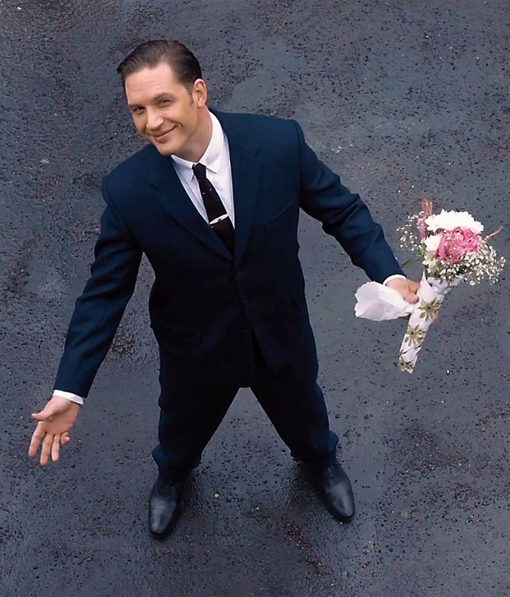 a man in a suit and tie holding a bouquet of flowers with his hands out