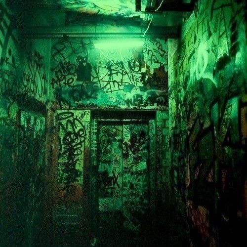 an alleyway with graffiti all over the walls and door to another room that is covered in green light