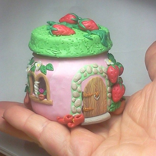 a hand is holding a small toy house with green and pink decorations on the roof