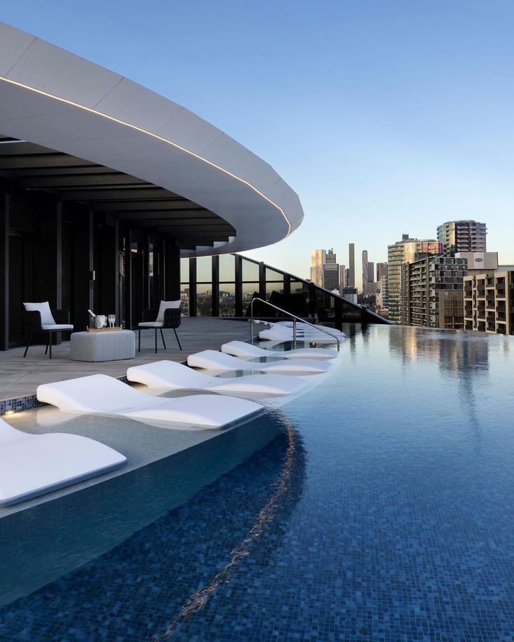 an outdoor swimming pool with lounge chairs next to it and the city in the background