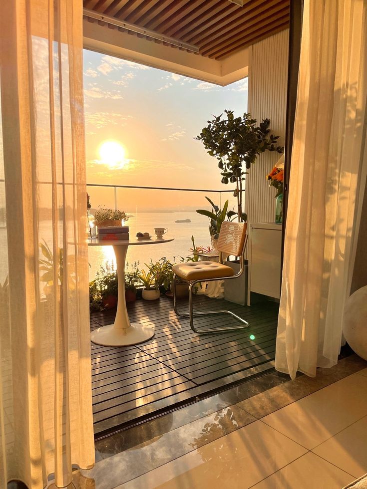 the sun is setting over the ocean from an open porch with chairs and potted plants