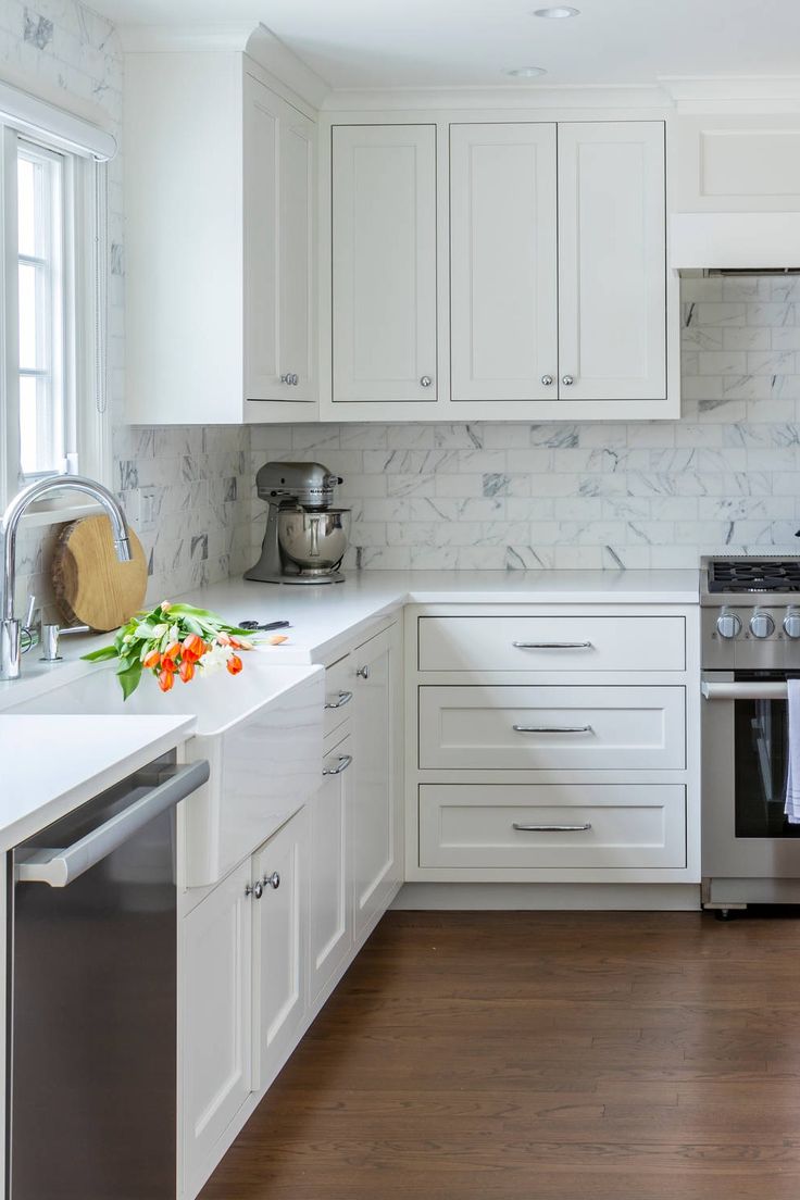 a kitchen with white cabinets and marble counter tops, an oven and dishwasher