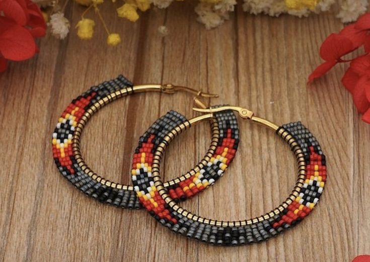 two hoop earrings with multicolored seed beads on a wooden table next to flowers