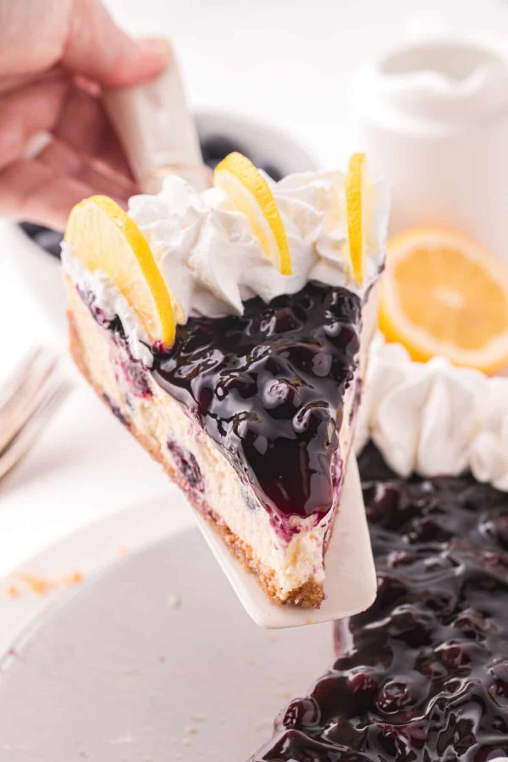 a piece of blueberry cheesecake being lifted from a plate with lemons and whipped cream